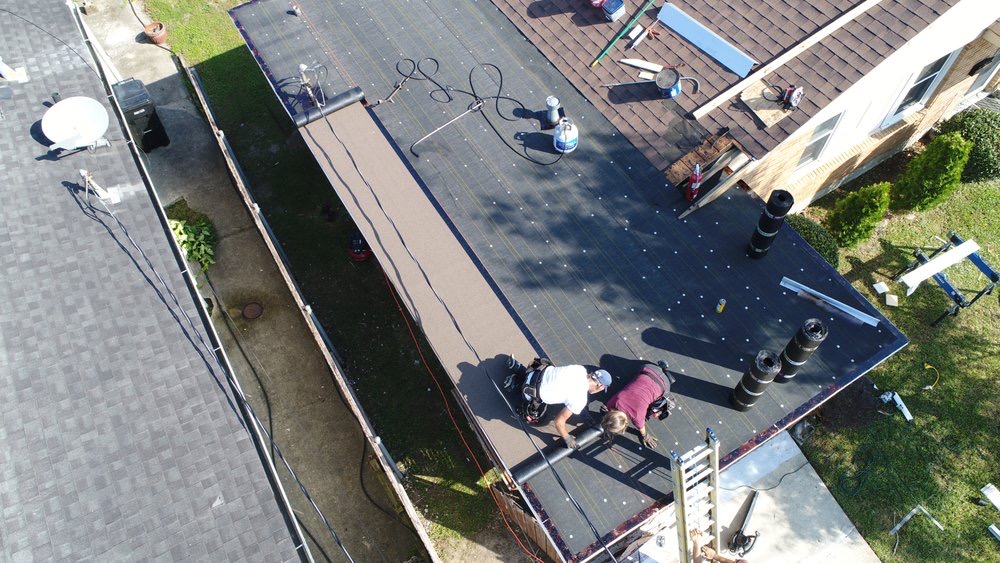 Crew installing underlayment on a flat commercial roof, aerial view